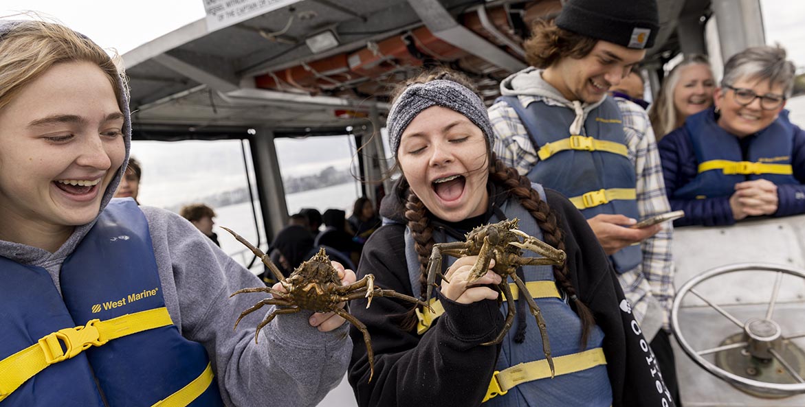 Two female students aboard a CBF education vessel exclaim over crabs they are holding.