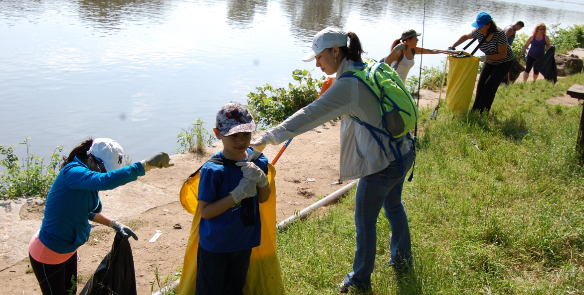 Group of people pick up trash along the banks of a river.