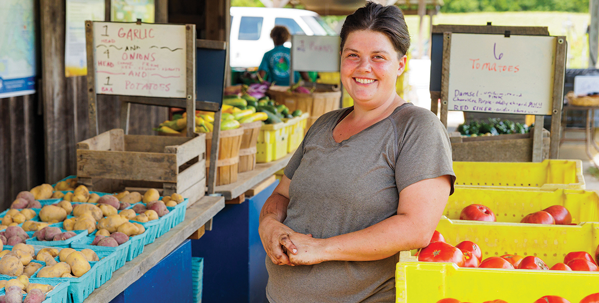 Woman standing among crates of fresh produce.