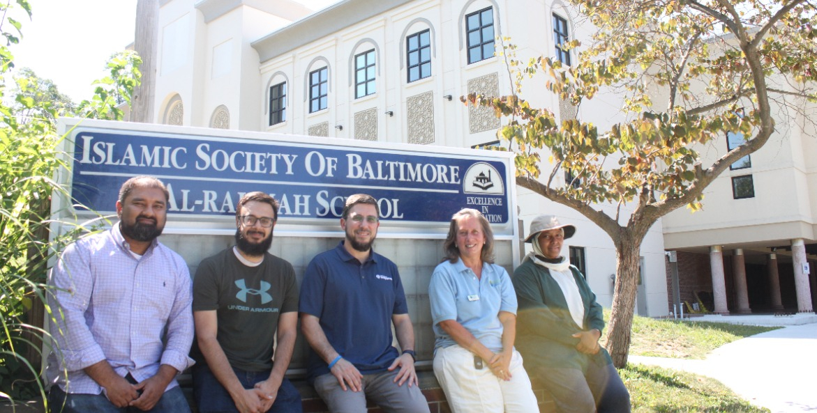 Five people sitting on a brick wall in front of the Islamic Society of Baltimore sign.