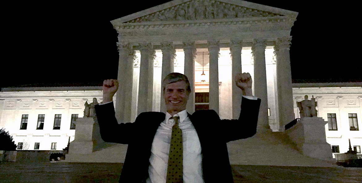 Man in a suite standing on the steps of the US Supreme Court building.