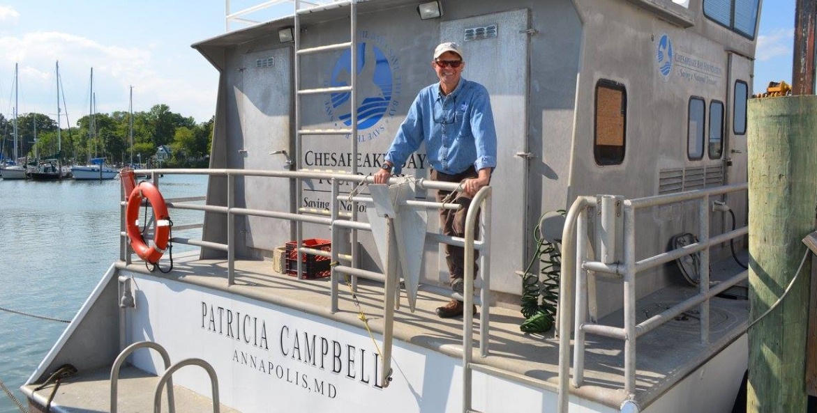 Man in a blue shirt standing at the railing of a large workboat.