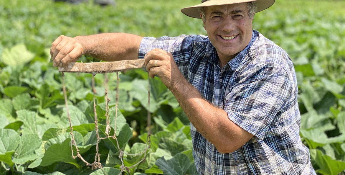 Man standing among plants on a farm holding the remains of clothing.