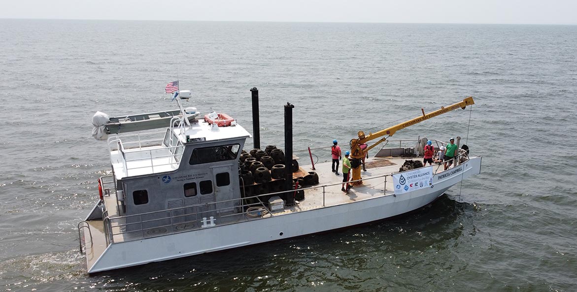 Overhead view of a boat with a crane and conveyor belt used in oyster restoration.