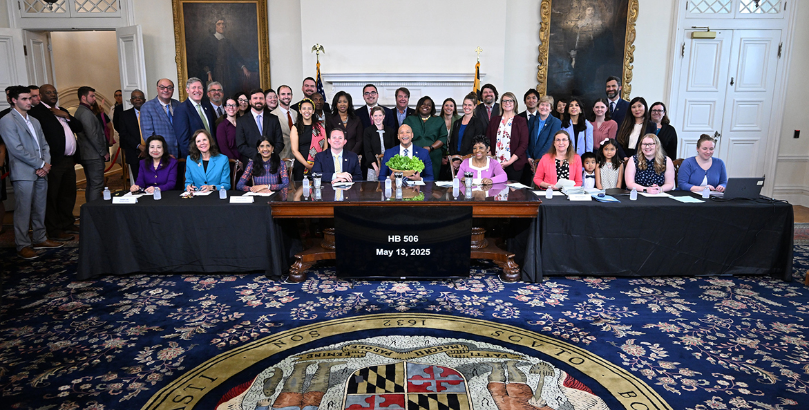 Gov. Moore at a desk, surrounded by smiling people