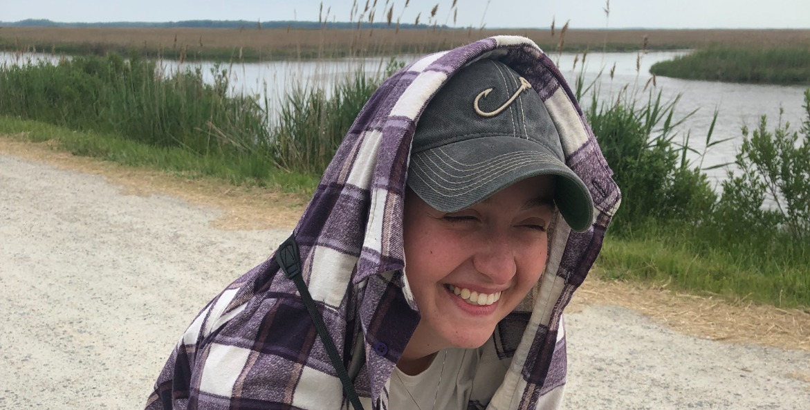 Woman on a dirt road with binoculars and her outer shirt covering her head.