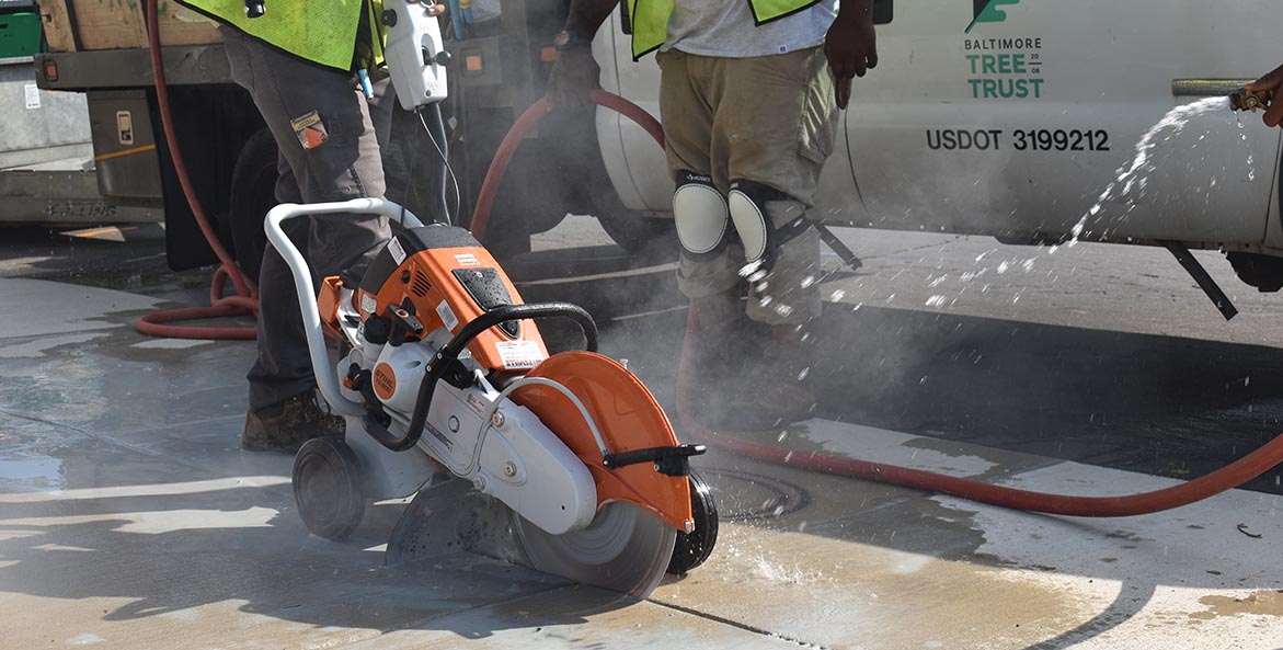 Two men cutting a hole in a sidewalk with a concrete cutter.