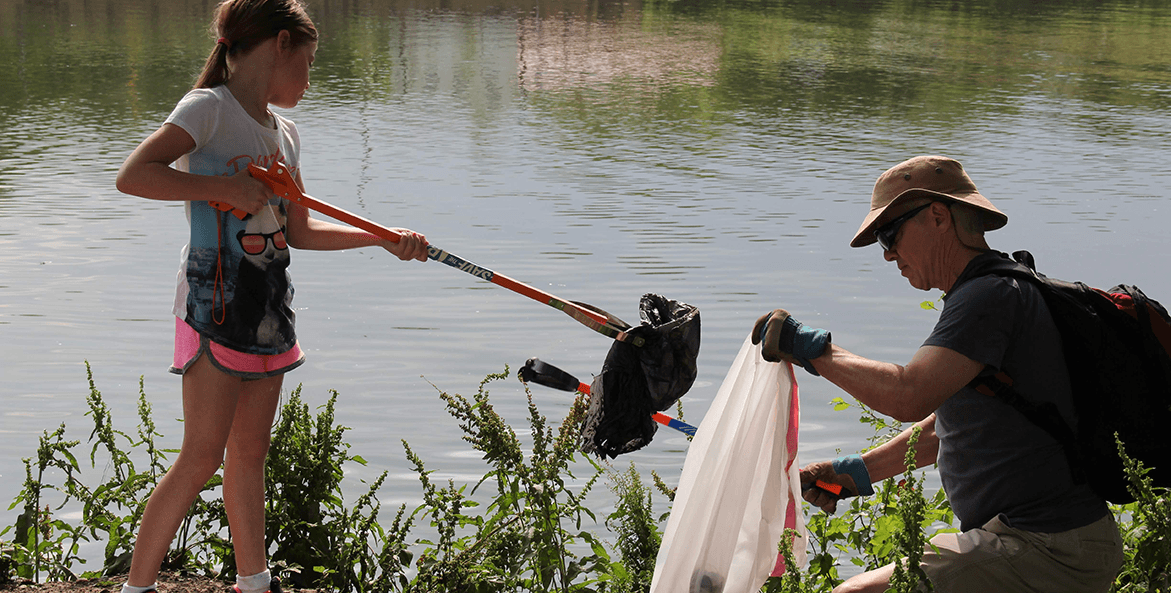 A man and young girl help pick up litter along the water