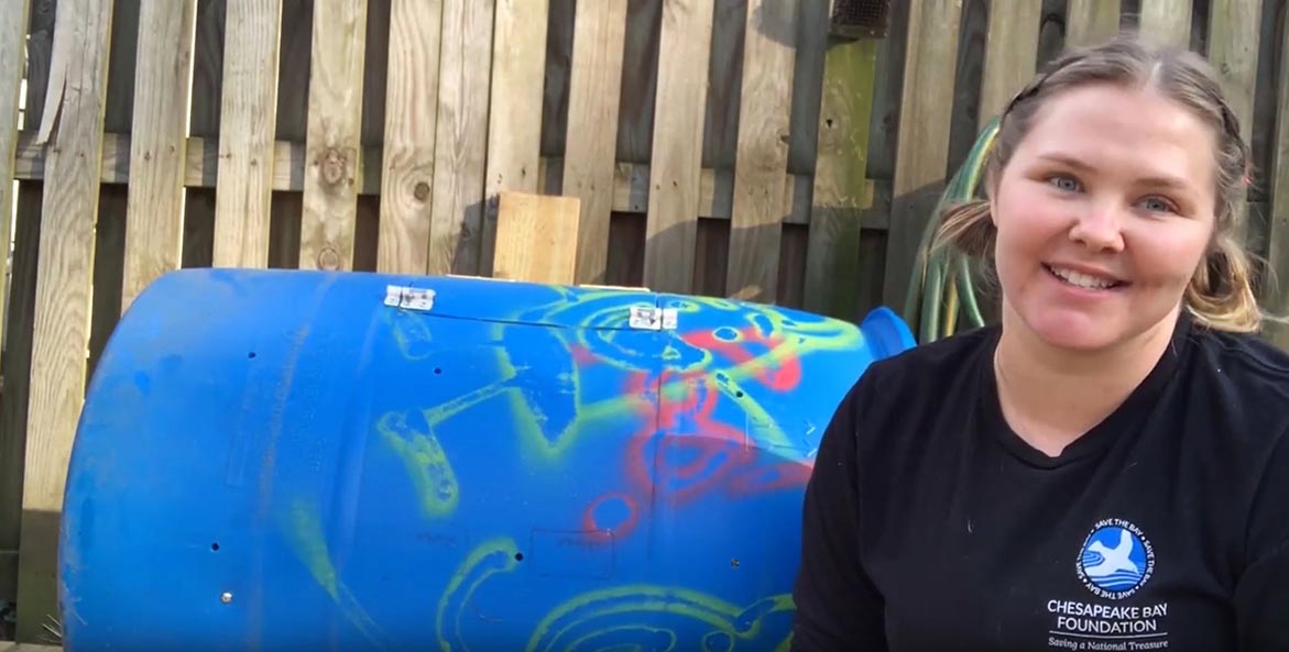 A woman stands infront of a brightly painted composting bin.