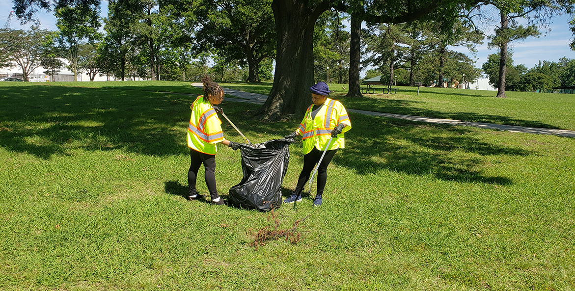 Two people pick up trash on the grass together