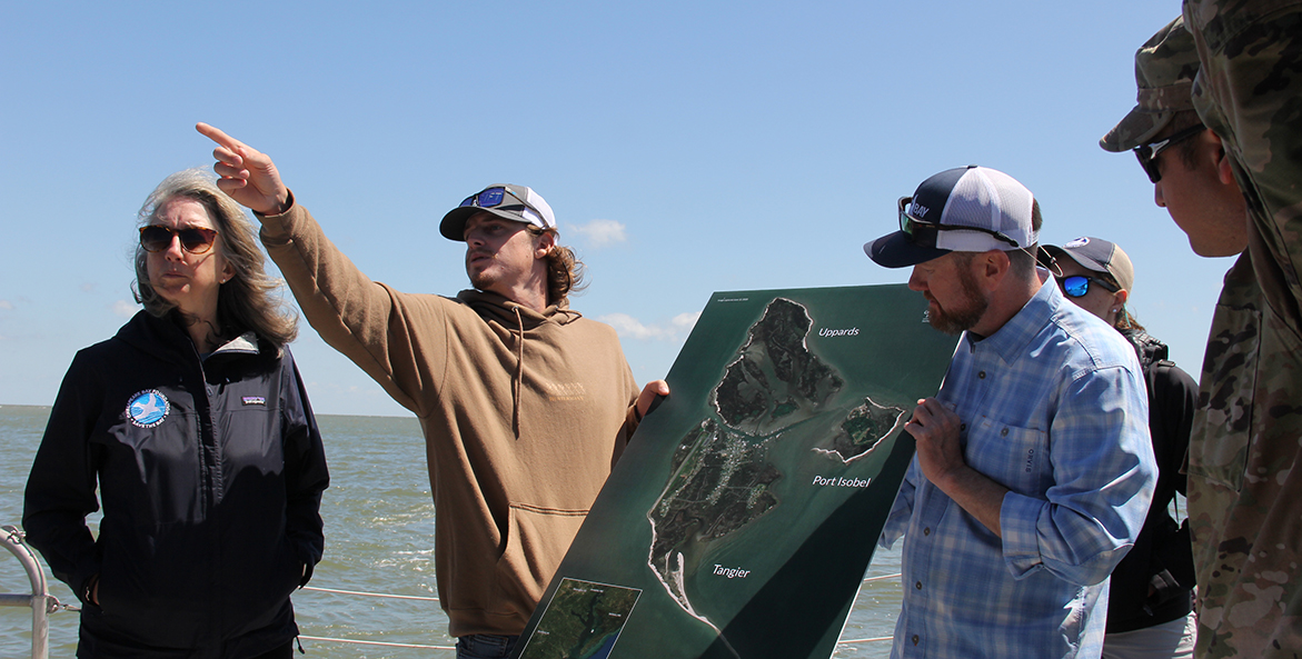 People stand on the water with a map of Tangier Island and point