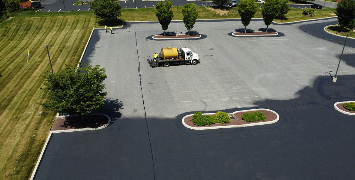 A truck moves through a parking lot applying pavement sealant.