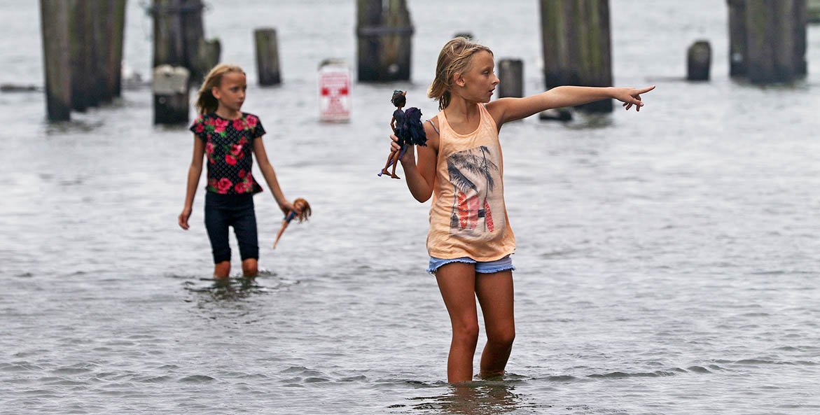 Two young girls walk through knee-high water.