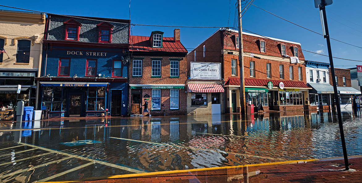 Floodwaters cover a parking lot and reach up to store fronts.
