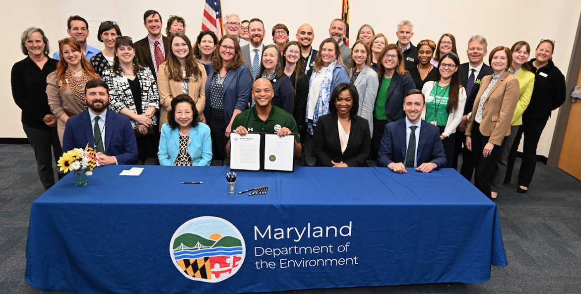 A group of people smile behind a Maryland Department of the Environment table, including Gov. Moore