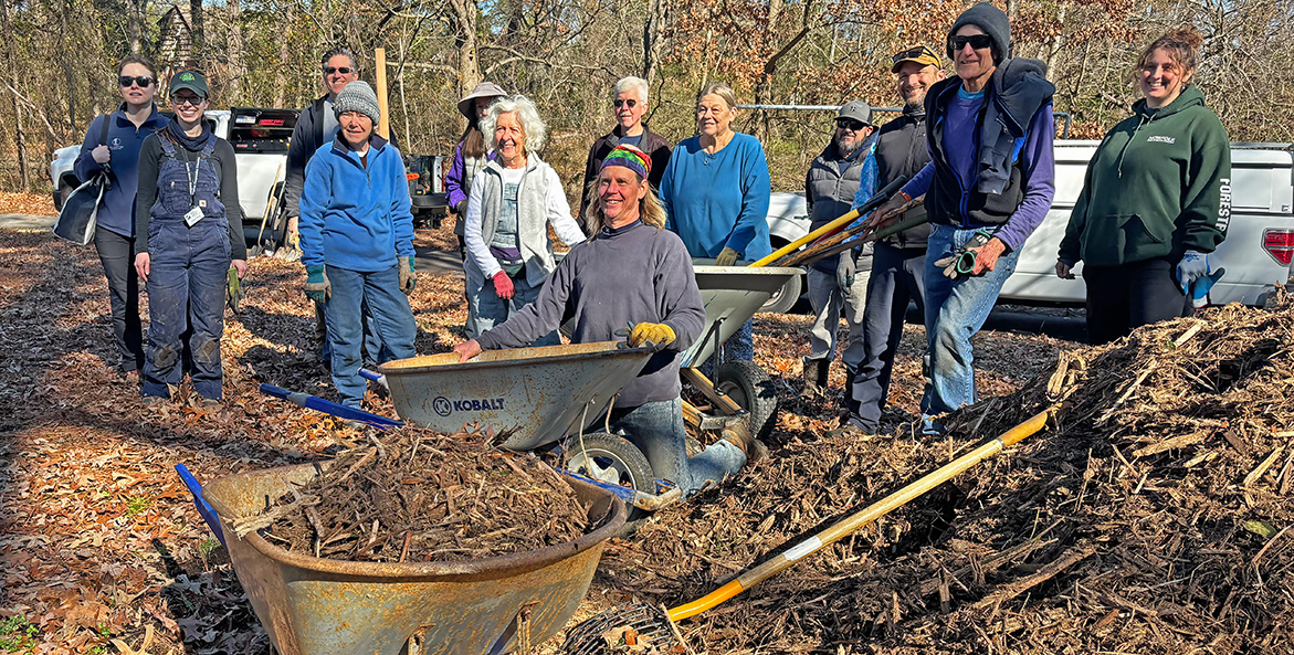 A group of volunteers pose around tools and supplies for tree planting.