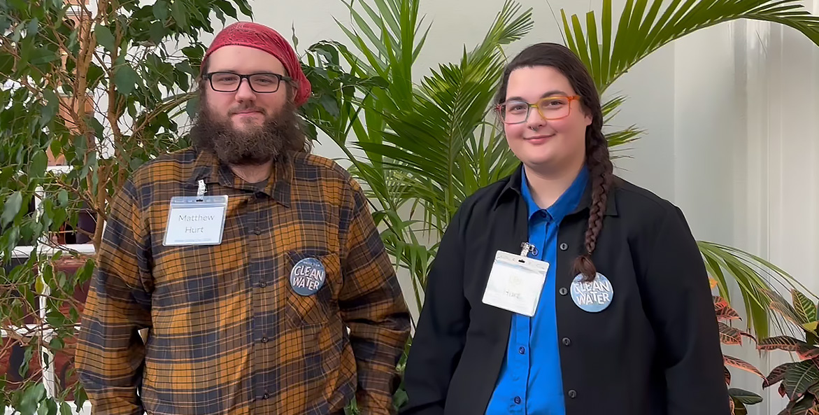 A man and woman stand together wearing name tags and Clean Water buttons.