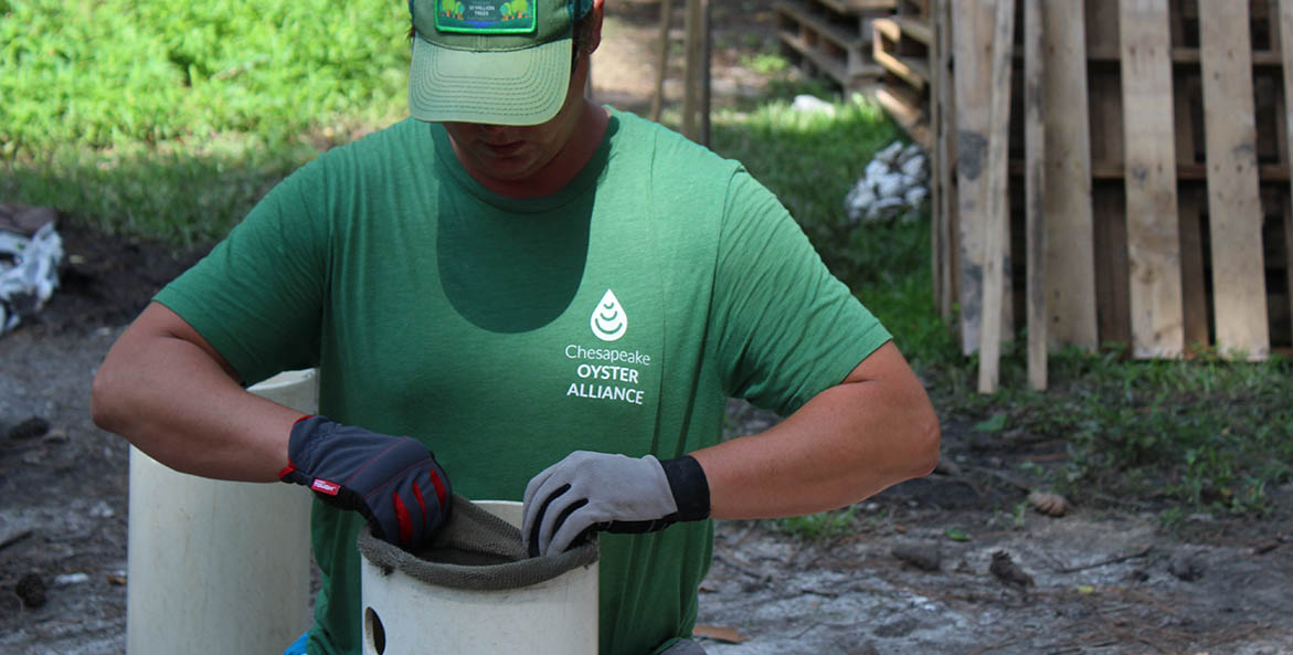 Man in a green shirt and hat setting up an oyster shell bag.