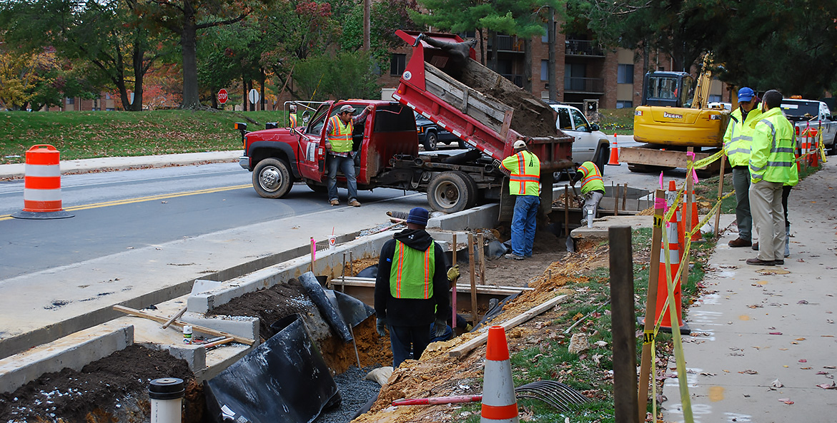 Construction workers working in a trench along a road.