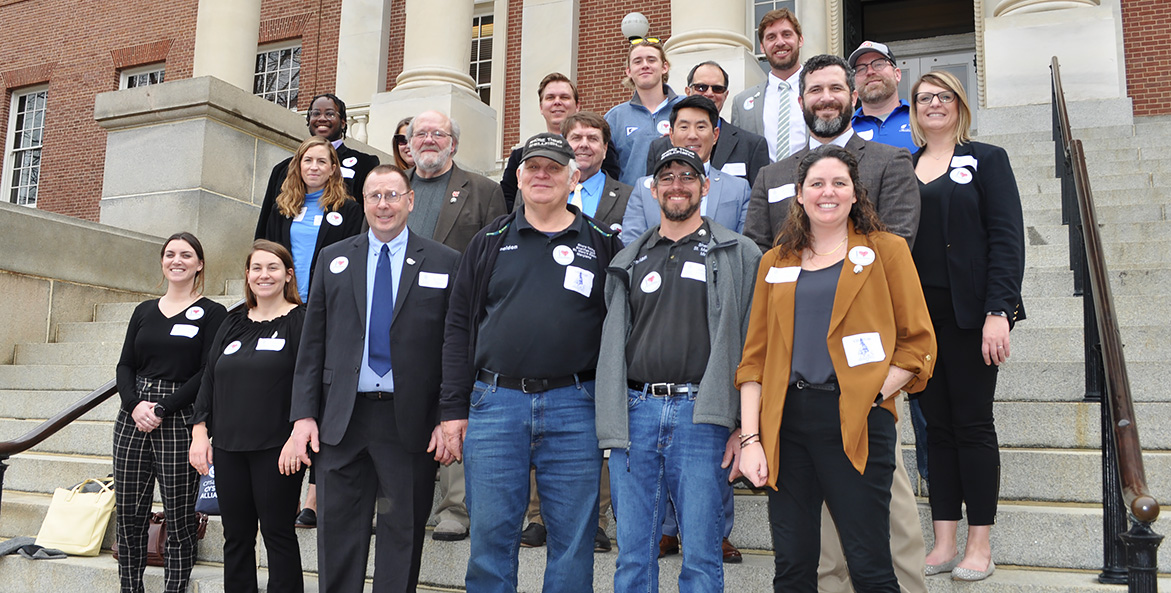 Nineteen people stand on the steps of the Maryland State House.