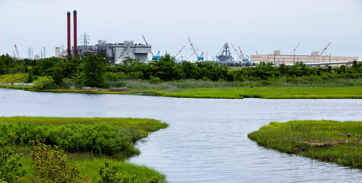 Creek running through wetlands with industrial factories in the background