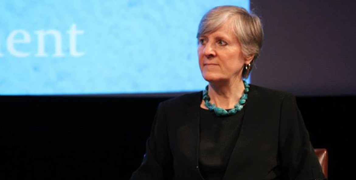 A person with short gray hair sits onstage for a panel