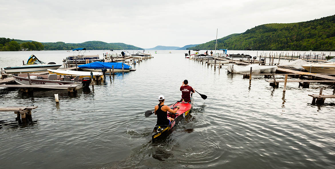 A couple of people canoing among docks and boats.