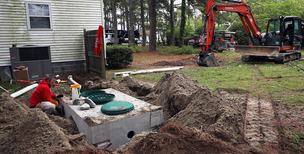 A white concrete septic tank is installed next to a house.