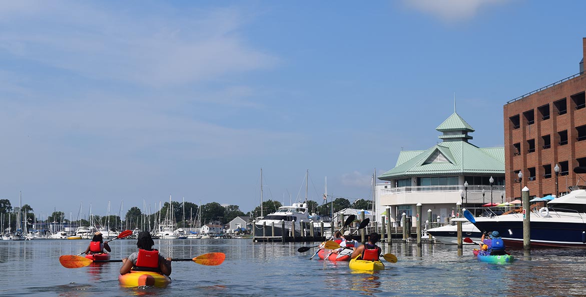 Several kayakers in colorful boats in a marina.