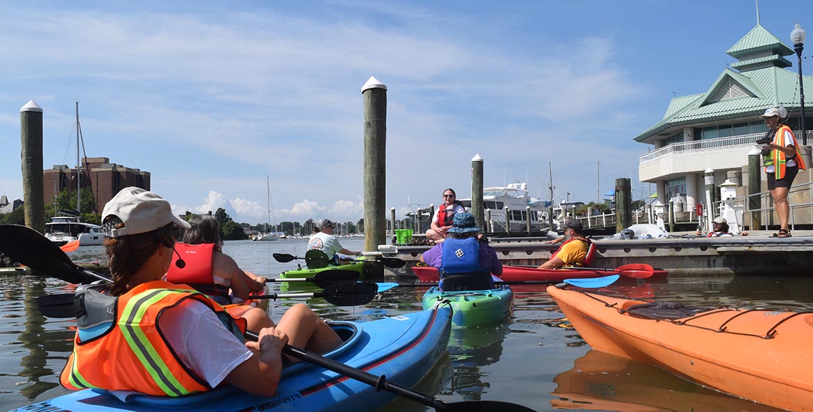 Kayakers in the water listenting to a speaker on a dock.