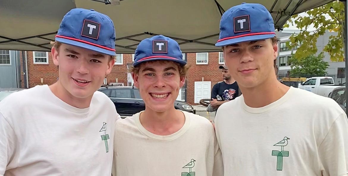Three young men in matching caps and t-shirts with a stylized T logo.