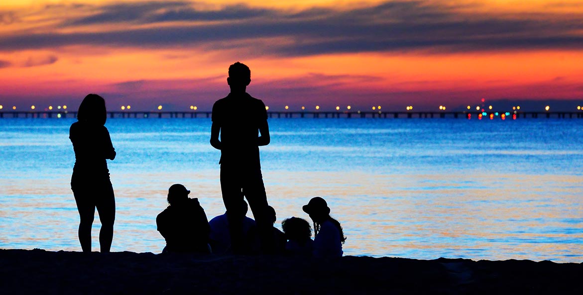 A family is silhoutted against an orange sunset.