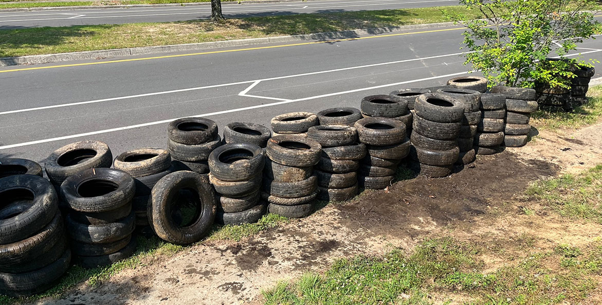 More than a hundred tires are stacked by a road awaiting pickup.