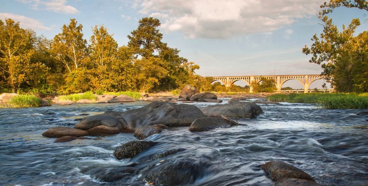 A river rushes over boulders in front of a large bridge