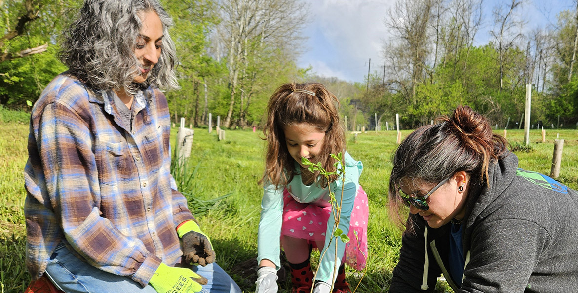 Two adults and a child plant a tree together