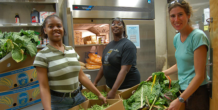 Three volunteers hold boxes of fresh green beans and greens.