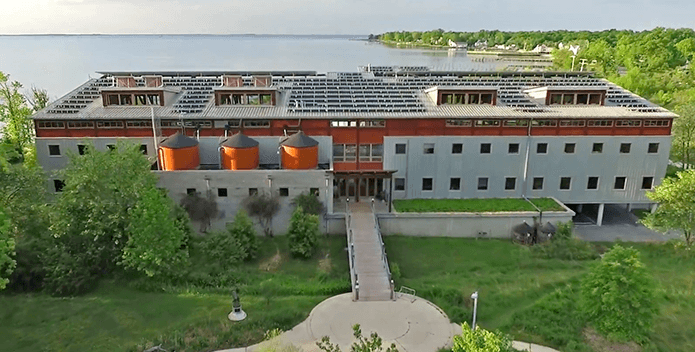 An aerial photo of the Philip Merrill Center shows the solar array covering the roof. The Bay lies beyond.