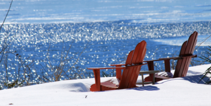 Image of two adirondack chairs on a blanket of snow on the ground.