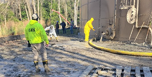 Several individuals stand next to a tank, with sludge on the ground.