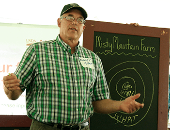 A man stands infront of a chalkboard, making a presentation.