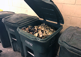 A green trash bin's open top reveals that it is full of oyster and clam shells.