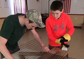 Eagle Scout helps younger Boy Scout assemble an oyster cage.