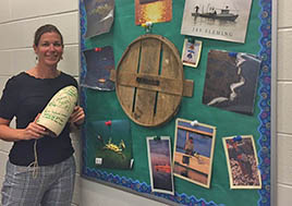 A woman stands in front of a bulletin board in a school hallway holding a white buoy. 