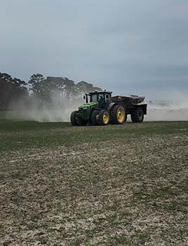 A photo of a tractor spreading fertilizer. 