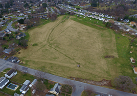 In an areial shot, a large grass field sits in the middle of a neighborhood.