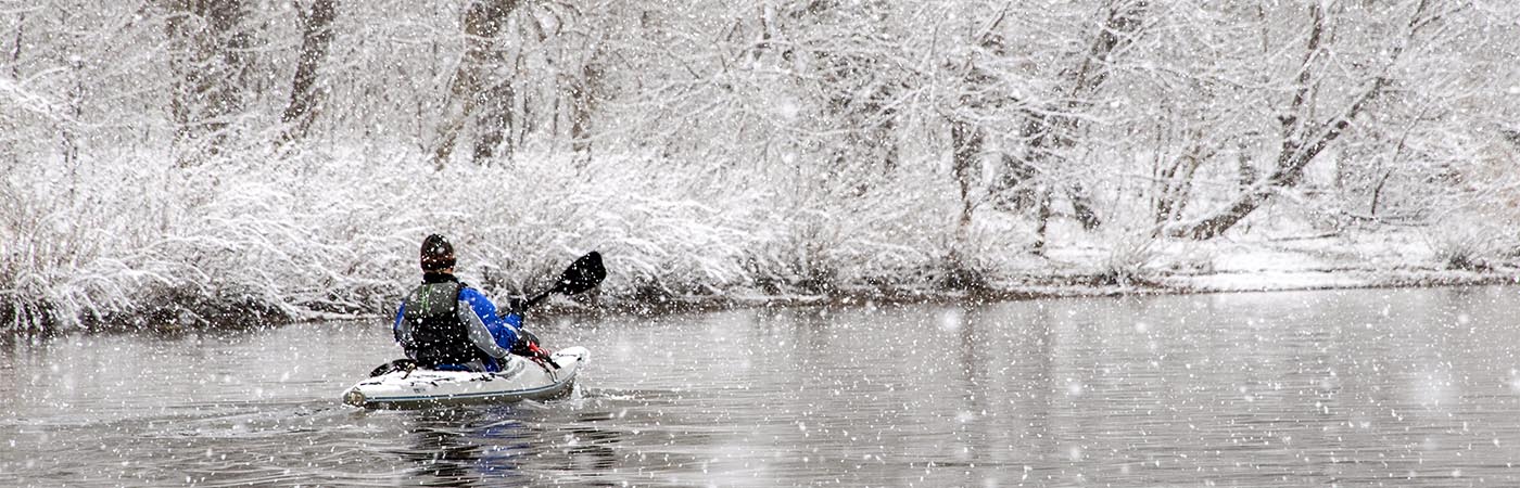 A kayaker enjoys a peaceful paddle surrounded by snow covered banks.