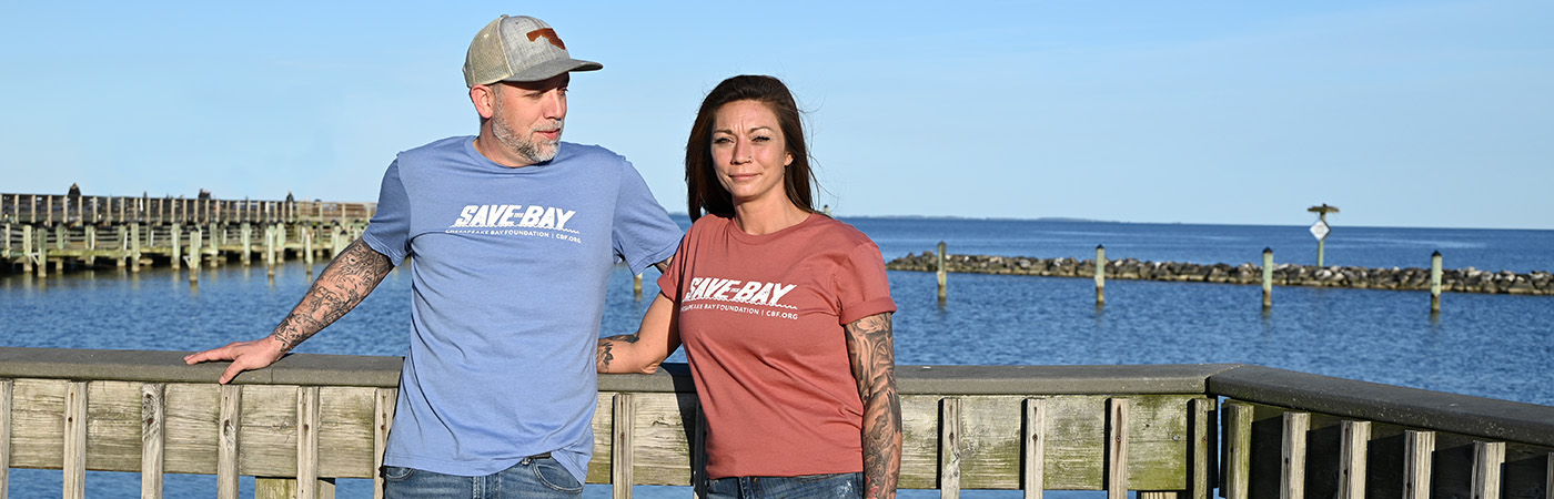 Man and woman stand together on dock wearing t-shirts that say Save the Bay.