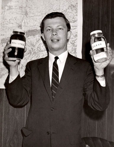 Older photo of a man in a suit holding two jars of water; once polluted and one clean..