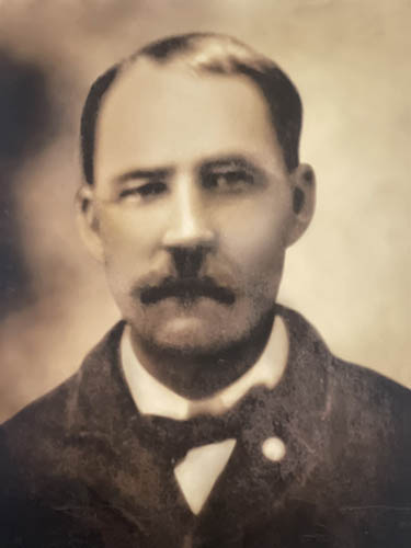 Antique portrait photo of a man in a dark jacket and bow-tie.