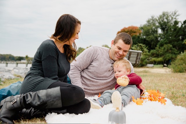 A woman, man, and baby lie on a blanket on the grass. 